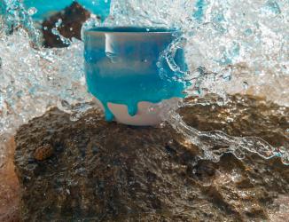 porcelain cup sitting on a jaggd ston by the sea with th ocean splashing around it