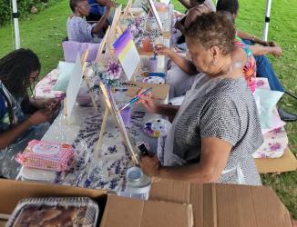 Artist Taniki Anderson leading an outdoor paint and picnic workshop with participants painting.