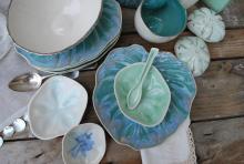 Image of handmade porcelain dinnerware in shades of teal, aqua, white and misty blue arranged in stacks on a weathered wood table