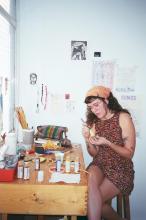 Milena sentada trabajando con diversos materiales sobre un escritorio.